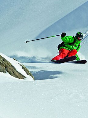 A person in a green jacket and red pants is skiing down a snow covered slope